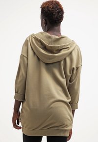 Sudadera con capucha de color verde oliva, corte holgado, capucha grande, mangas tres cuartos y tejido suave con textura. Cuenta con un dobladillo redondeado.