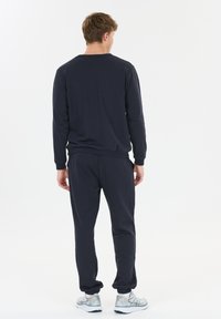 Donkerblauwe sweat suit gemaakt van zachte stof, met een crew neck shirt en elastische manchetten, gecombineerd met bijpassende joggers en stijlvolle sportieve schoenen.