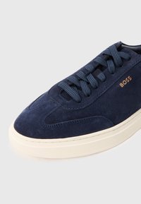Baskets en daim bleu marine avec bout arrondi, design à lacets plats, coutures visibles et semelle en caoutchouc blanche contrastante. Texte « BOSS » en accent doré.