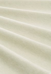 Hellbeige Stoff mit glatter Textur, der sanfte Wellen und Falten zeigt und das weiche, baumwollähnliche Material betont.