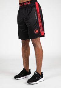 Zwarte sportshorts met rode accenten, voorzien van een ritszak, elastische tailleband en "GORILLA WEAR" gedrukt langs de zijkant.