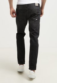 Černé džíny z denimu s úzkým střihem, pěti kapsami, jemným vyblednutím a bílou koženou nášivkou na zadním pásku. Kombinovány s bílými teniskami.