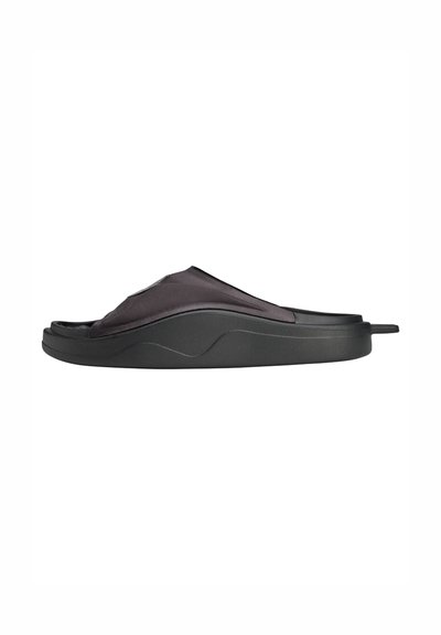 Svart slidesandal med en mjuk, strukturerad ovandel, en formad sula och en böjd design. Har en minimalistisk stil utan synlig hårdvara.