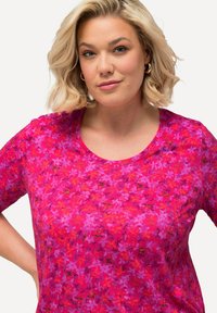 Camiseta de manga corta en un vibrante color rosa con un patrón floral, con un escote redondo y una textura suave. El diseño incluye tonos de magenta y rojo.