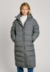 Garšs pelēks pūka mētelis ar kapuci, ar quilted dizainu, lieliem pogām un sānu kabatām. Valkāts virs balta ribota džempera.