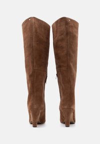 Ζευγάρι ψηλές καφέ μπότες από σουέντ με μεσαίου ύψους τακούνια, με διακριτικές ραμμένες λεπτομέρειες και φερμουάρ στο πίσω μέρος, σε θέα από πίσω.