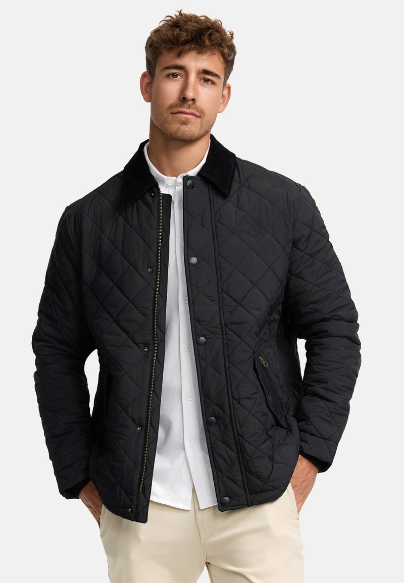 Quilted svart jakke med kordfløyelskrage, som har trykknapper, sidelommer og en lett strukturert overflate.