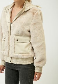 Faux fur bomberjakke i creme, med en glat læderlignende indvendig, to forlommer og ribbede manchetter og kant.