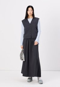 Dark gray sleeveless vest with front buttons over a light blue long-sleeve top; model wears a long black skirt and gray platform shoes.