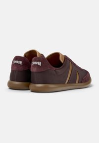 Sneakers maroon dan cokelat dengan tekstur jala dan suede, menampilkan logo "Camper" di belakang. Pandangan samping menunjukkan desain tali sepatu.
