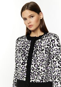 Cardigan animalier in bianco e nero con accenti lilla, caratterizzato da un colletto rotondo, chiusura a bottoni e orlo aderente.