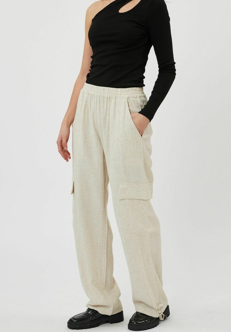 Pantaloni cargo beige chiaro con due tasche laterali, vita elastica e polsini regolabili con cordoncino. Abbinati a un top nero a spalla unica.