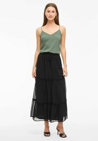 Zwarte maxi rok met witte stippen, bestaande uit drie lagen, met een elastische tailleband en trekkoord. Gepaard met een mouwloze groene top met dunne schouderbandjes.
