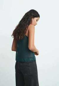 Top smanicato di un blu scuro con tessuto trasparente e orlo a pois, abbinato a jeans scuri a vita alta. Design minimalista.