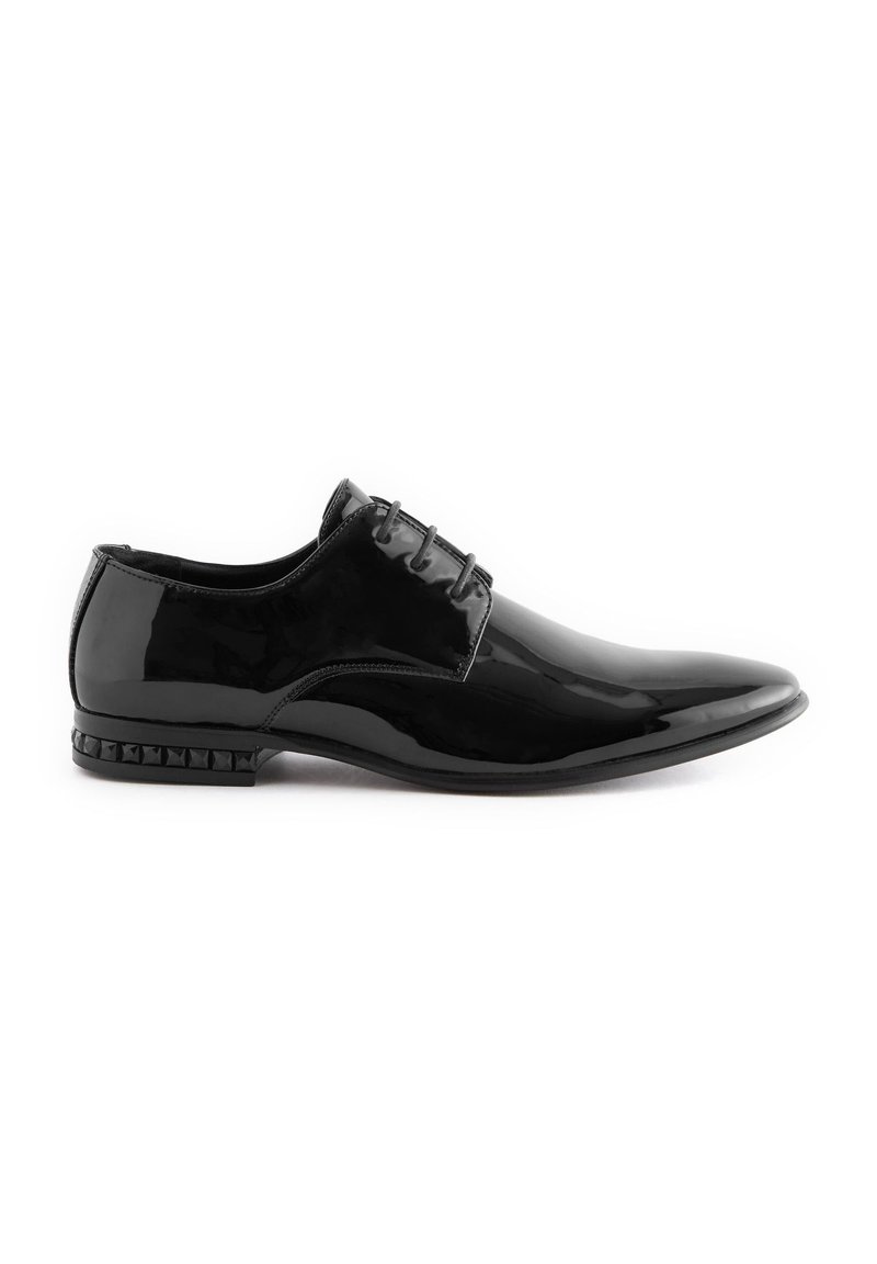Chaussure habillée en cuir verni noir avec un bout pointu, un design à lacets à quatre œillets et un accent de talon clouté. Texture lisse et finition brillante.