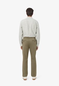 Koszula z długim rękawem w paski w jasnej zieleni i bieli, zestawiona z oliwkowozielonymi spodniami. Spodnie mają elastyczną talię i boczne kieszenie.