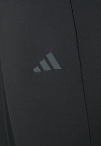 Leggings sportivi neri con una texture liscia, un design aderente e un logo adidas grigio riflettente vicino alla coscia.