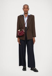 Blazer oversized castanho, camisa azul clara, calças largas azul marinho e uma pequena bolsa bordô. Sapatos pretos com detalhes em dourado.