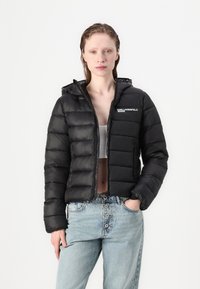 Juoda pūkinė striukė su gobtuvu, su užtrauktuku priekyje ir siuvinėta dygsniuota konstrukcija. Kairėje krūtinės pusėje yra logotipas, o rankogaliai yra elastingi.