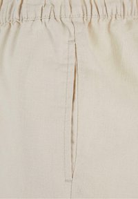Gros plan sur un tissu beige avec une ceinture élastique et une poche verticale fendue sur le côté.