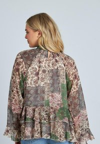 Blusa a strati con motivi di patchwork in verde, mauve e crema. Caratterizzata da un orlo arricciato e apertura a chiave sul retro. Tessuto trasparente e leggero.