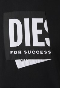 Tessuto nero con una toppa quadrata con testo bianco audace: "DIES FOR SUCCESS" e un'altra etichetta bianca più piccola che spunta sotto.