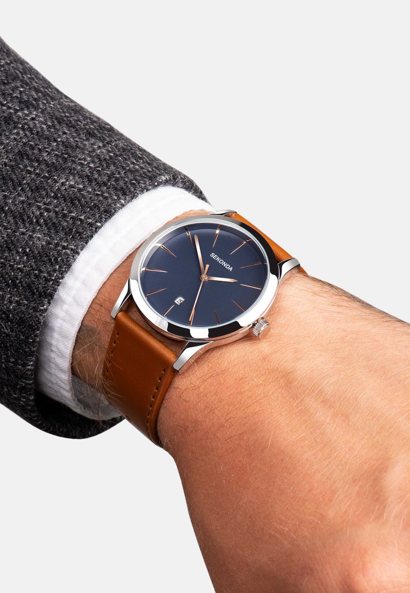 Montre ronde avec un cadran bleu marine, un boîtier en argent, des accents en or rose et un bracelet en cuir marron, dotée d'un guichet de date à 6 heures.