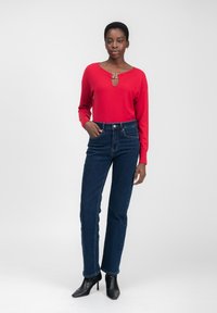 Rode lange mouwen sweater met een sleutelgat-halslijn, gecombineerd met hoge taille donkerblauwe denim jeans en zwarte puntige hakken.