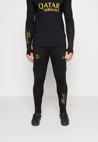 Černá sportovní souprava obsahující dlouhý rukáv s žlutým logem "Qatar Airways" a odpovídající legíny s nápisy "Paříž" a logy týmu, zvýrazněný design.