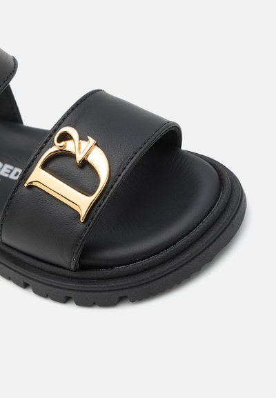 Sandales en cuir noir avec une large sangle et un accent logo doré proéminent. Présentent un semelle intérieure texturée et une semelle en caoutchouc noir durable.