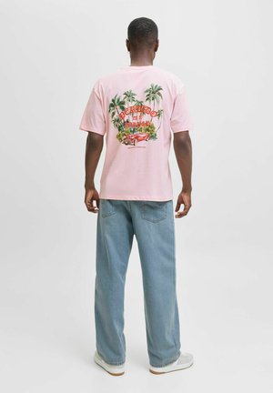 Roze katoenen t-shirt met een grafische print met palmbomen en een auto. Gepaard met lichtblauwe baggy jeans en grijze sneakers.