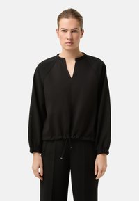 Černý pulovr s výstřihem do V, elastick�ými manžetami a stahovací šňůrkou v pase. Hladká látka; volný střih. V kombinaci s odpovídajícími černými kalhotami.