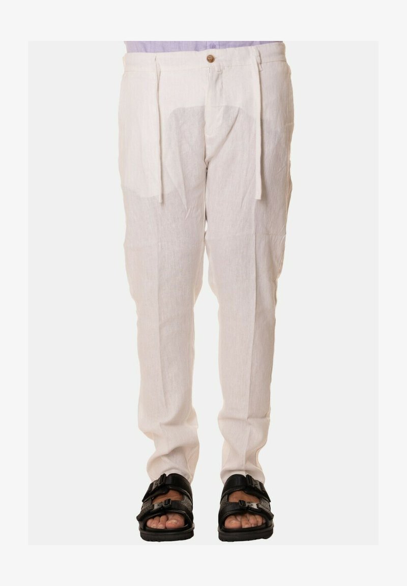 Pantaloni bianchi in lino con vestibilità rilassata, caratterizzati da una vita con cordoncino, pieghe frontali e un'unica chiusura a bottone. Indossati con sandali neri.