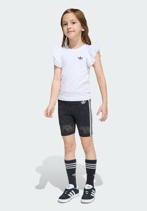 Camiseta blanca con mangas abullonadas de encaje, pantalones cortos negros con estampado y rayas blancas, calcetines negros hasta la rodilla y zapatillas negras con detalles en blanco.