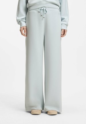 Person wearing light gray wide-leg pants with drawstring waist and beige moccasin-style shoes, standing against a white background.