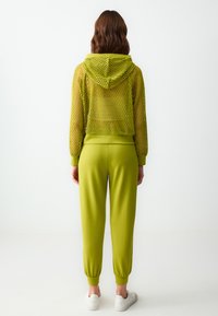 Grüne Netz-Haube-Cropped-Hoodie mit Kapuze und geripptem Saum, kombiniert mit passenden taillierten Jogginghosen. Glatte Textur und elastische Bündchen.