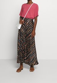 Svart kjol med färgglada diagonala ränder, ihop med en lös rosa topp och bruna platta sandaler. En liten vit handväska fulländar outfiten.