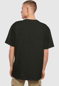 Zwarte kortlopende t-shirt gemaakt van katoen. Heeft een ronde hals en een relaxte pasvorm. Achteraan is de gladde textuur en minimale details zichtbaar.