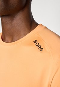 Oranges Sportshirt mit rundem Ausschnitt und glatter Textur, mit "BORG" in Schwarz auf der linken Schulternaht.