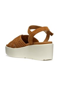 Sandali con zeppa in camoscio marrone, con tomaia intrecciata, cinturini regolabili e suola piatta bianca. Il design enfatizza la texture e la coerenza dei colori.
