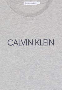 Grijze katoenen t-shirt met een ronde hals, voorzien van een groot, donkergrijs "CALVIN KLEIN" logo dat over de borst is gedrukt. Maatlabel zichtbaar.