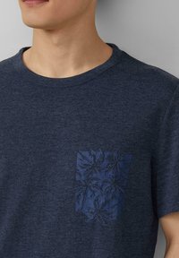 Marineblauwe katoenen t-shirt met een ronde halslijn en korte mouwen; voorzien van een getextureerd palmenbladpatroon op het linkerdeel van de borstzak.