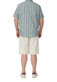 Kurzärmeliges Hemd in Hellblau mit einem Palmenmotiv; kombiniert mit weißen Shorts und hellen Schuhen. Lässiger, atmungsaktiver Stoff.