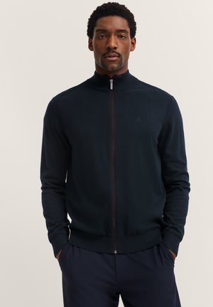 Maglione zip-up blu scuro con colletto alto, polsini e orlo a costine. Il tessuto sembra morbido con una leggera texture. Piccolo logo sul petto.
