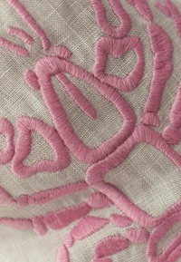 Gros plan d'un tissu avec broderie rose en relief formant des formes géométriques et en cœur sur un tissu beige tissé.