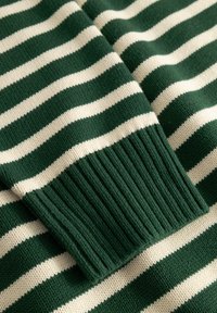 Tissu tricoté à rayures horizontales vertes et blanches avec un détail de poignet côtelé, montrant de près la texture et le motif.