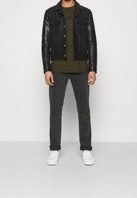 Chaqueta de cuero negra con dos bolsillos en el pecho, camiseta verde oliva con logo, jeans grises y zapatillas blancas. Diseño simple y minimalista.