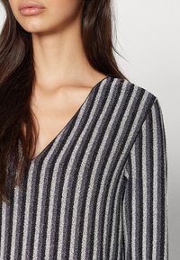 Haut noir et argent avec des rayures, au design en V, présentant un tissu texturé et des manches longues qui créent un intérêt visuel.