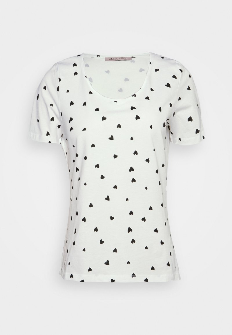 T-shirt blanc à manches courtes avec un col rond et un motif de petits cœurs noirs sur l'ensemble. Fabriqué en tissu coton doux.