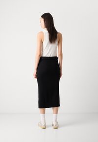 Jupe midi noire en tricot avec un ourlet côtelé, associée à un débardeur blanc et des baskets légères, avec des chaussettes de longueur cheville.
